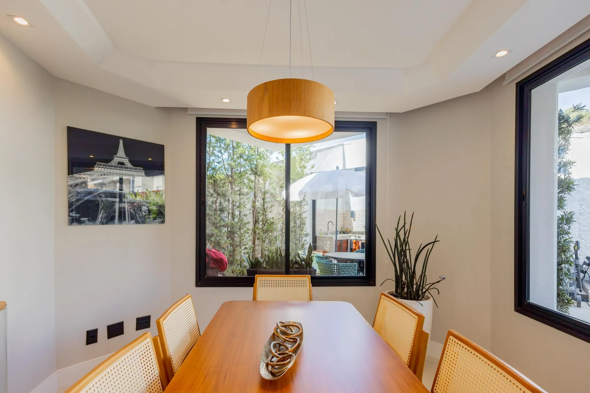 Sala de jantar com pendente de madeira e janela para o jardim