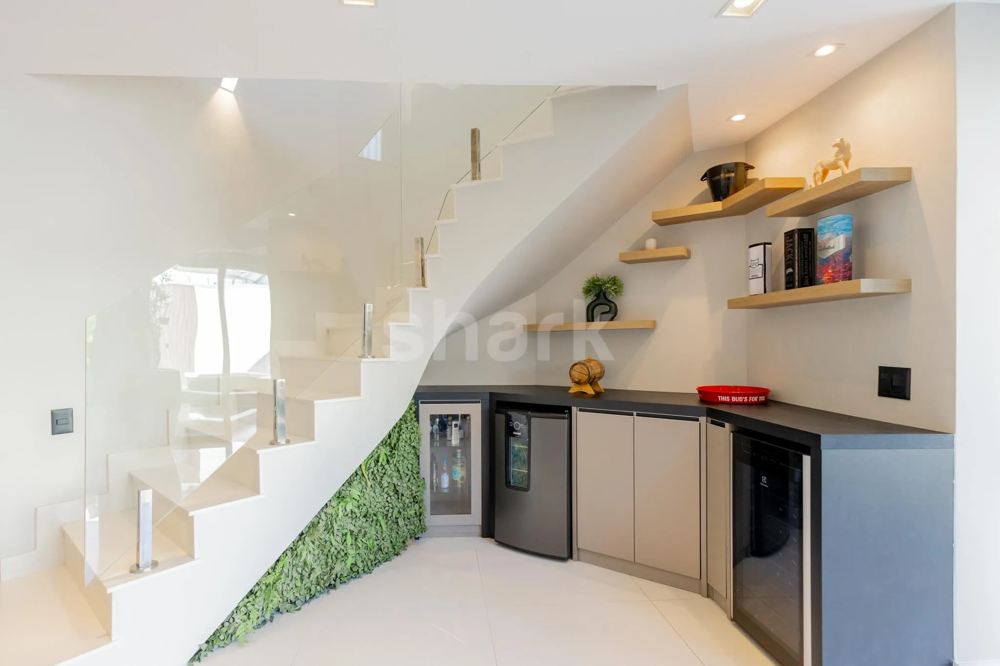 Adega e frigobar embutidos sob a escada, com jardim vertical ao lado
